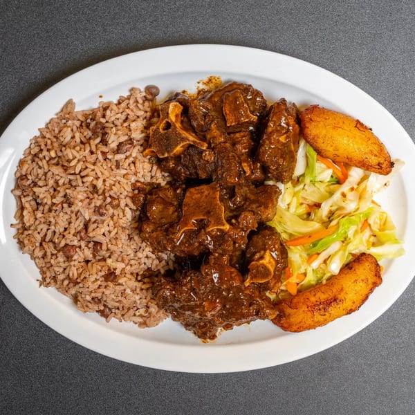 Oxtail stew with rice and peas, steamed cabbage, and fried plantains on a white plate.