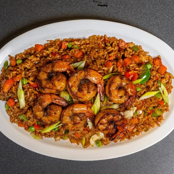 Shrimp fried rice with carrots, peas, and bell peppers on a white oval plate.
