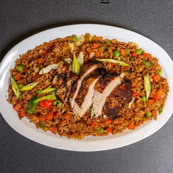 Grilled chicken slices on a bed of fried rice with vegetables, garnished with green onions.