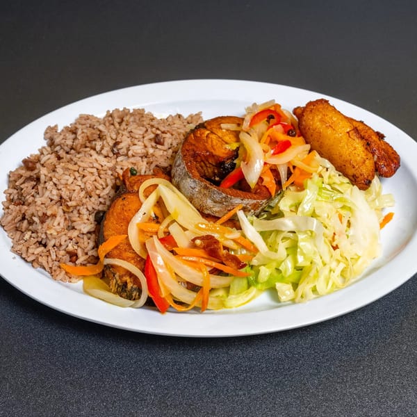 A white plate with brown rice, fried fish, pickled vegetables, cabbage, and plantains.