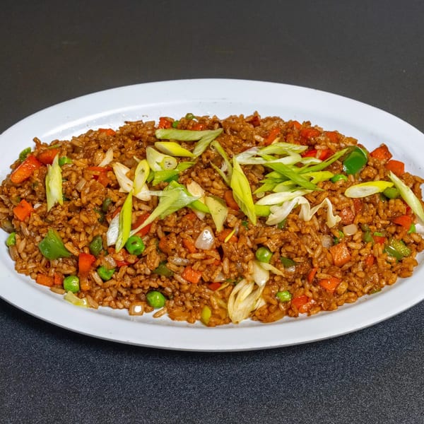 A white oval plate filled with vegetable fried rice, garnished with sliced green onions.
